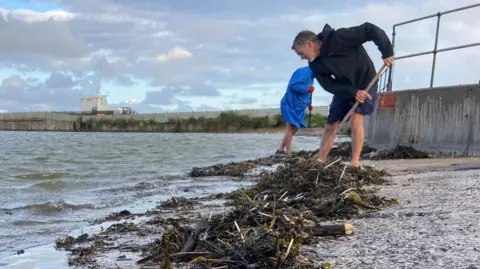 LDRS Two volunteers are seen clearing away rubbish and seaweed at the edge of New Brighton marine lake