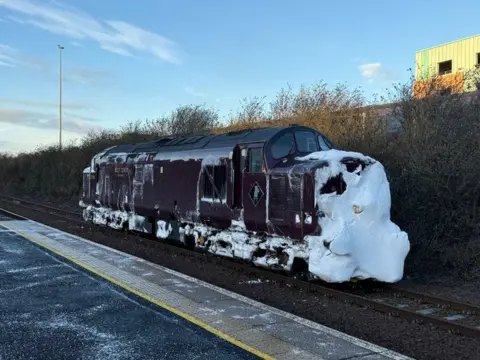 Network Rail Una locomotora de color rojo oscuro con nieve acumulada en la parte delantera