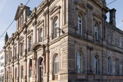 Vox Media Canada House is a Victorian stone building, five storeys high with ornate windows, brickwork and two statues overlooking the front entrance