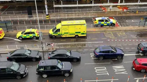 Cars are held in a queue while police and other emergency services respond to an incident at Heathrow Terminal 3 with an ambulance and some police cars seen