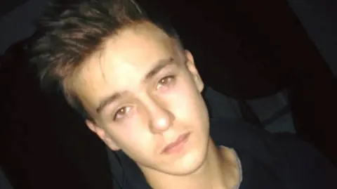 Photo of stabbing victim Denva Smith. He is looking stoney-faced with gelled up hair. He is wearing a black jumper.