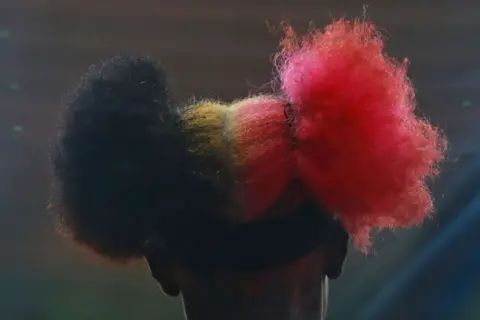 CARLOS SANTIAGO / GETTY IMAGES A woman wears her hair in two puffs - one is black, the other is pink.