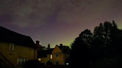 Dedham Vale National Landscape Dark Skies campaign Picture shows several homes and trees. The sky is a dark lilac colour with stars.