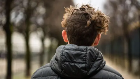 Rear view of teenage boy looking down along a vanishing point of rows of trees in a park