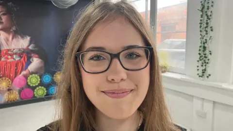 Nadia smiling at the camera. She has long fair hair and is wearing a black top and glasses.
