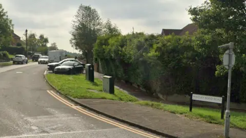 A street sign for Whitley Wood Road in Reading, the start of a residential road, with cars parked aside the road. 