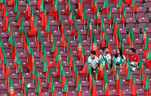Getty Images Four Portugal fans sit in an empty stadium filled with Portuguese flags neatly placed between the seats.