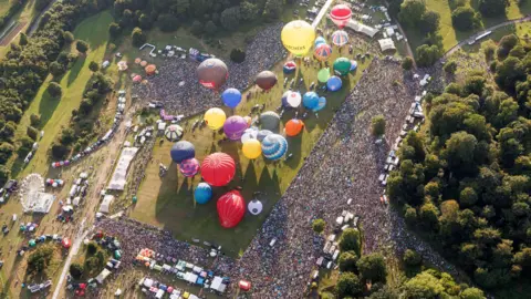 Paul Box The Bristol International Balloon Fiesta 2024 site is seen from above. Thousands of people can be seen surrounding the main arena, where multiple balloons are inflated ready to take off. Stalls, other tents and vehicles can also be seen around the edge of the site