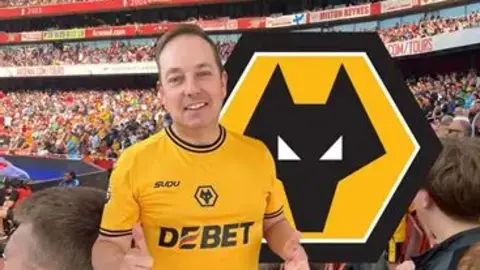 Dazzling Dave/Always Wolves Fan TV A man with short brown hair smiles at the camera and puts his thumb up. He is wearing a Wolverhampton Wanderers shirt. The background is of a football crowd. There is also a Wolves badge super imposed on the photo.