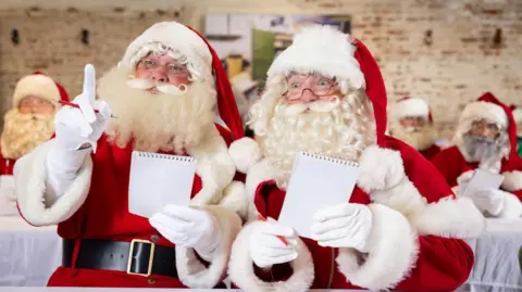 PA Media A picture of multiple men dressed as Santa Clause. There are two prominent men who are holding a piece of paper and looking of to the distance, with one of the Santa's holding his finger up.