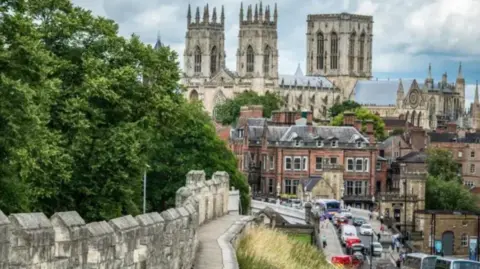 This is a classic shot of York Minster from the city's walls. It was taken from the stretch of the walls near to the railway station. Lendal Bridge across the River Ouse is busy with traffic in both directions.