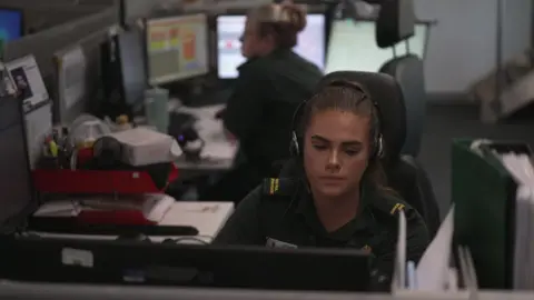BBC Emergency 999 call handlers in an office sitting at computers with headsets on their heads.