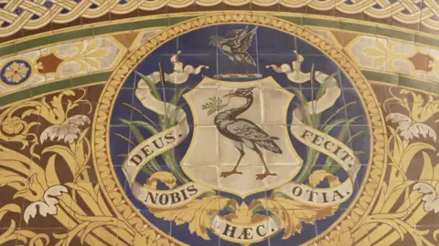 A bird depicted on the tiled floor surrounded by blue and yellow tiles and latin writing