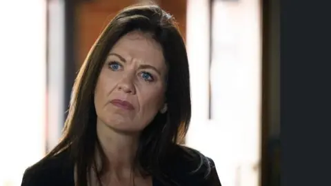 A woman with long brown hair is appearing to be concentrating on something in the room.