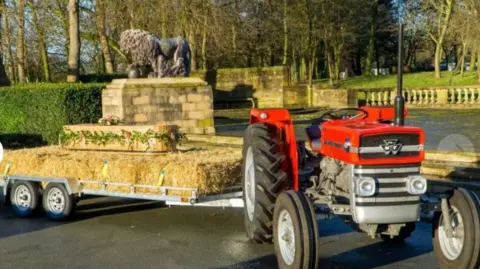 Fylde Funerals A small red Massey Ferguson 135 tractor with a trailer of hay bales attached