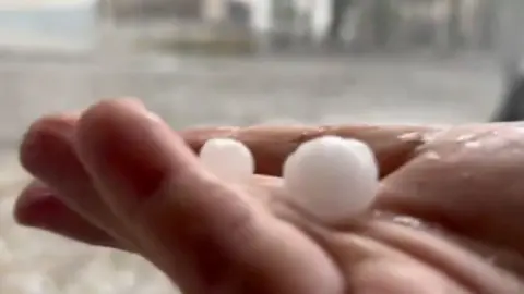 A woman holds hailstones in her hand