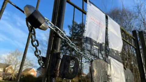 Stuart Woodward/BBC A metal gate with a padlock through the bars. On the gate are three pieces of A4 paper which are eviction notices