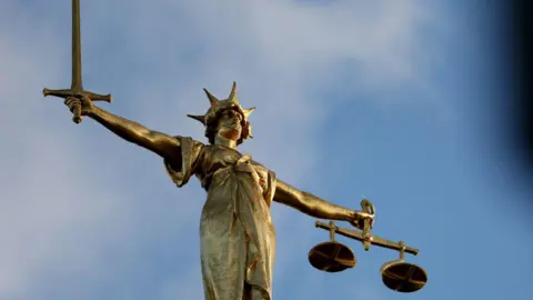 A close up of the statue of justice on top of the Old Bailey court building, a classical female figure rendered with a sword held aloft in one hand and a set of scales in the other hand. 