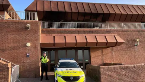 A police officer standing beside a police car outside the red bricked Bournemouth International Centre.