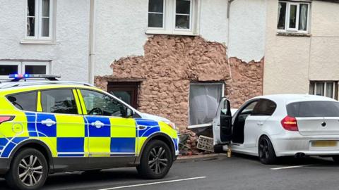 A police car parked next to the white Volkswagen and the hole in the house it left