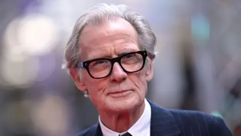 Getty Images Actor Bill Nighy wears a smart navy pinstripe suit and bold black glasses on the red carpet at the London Film Festival