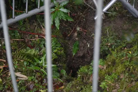 National Trust - Lucy Fenna Grey fences cordon off a hole in the dirt