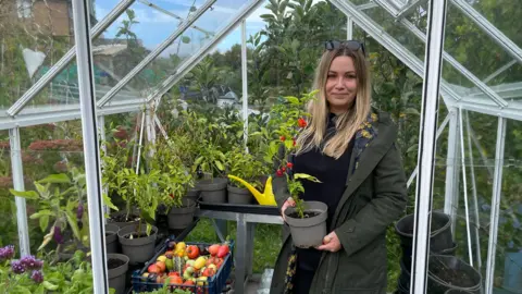 A woman wearing a green coat in a greenhouse holding Carolina Reaper pepper plant. 