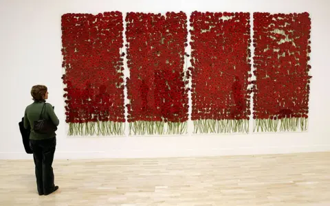 Getty Images A woman looks at four wall hangings made up of deep red poppies