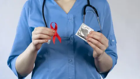 Medical professional holding red ribbon and condom