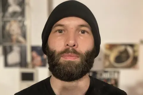 Tenant, Danny Iles, wearing a black beanie hat, black t-shirt and brown beard