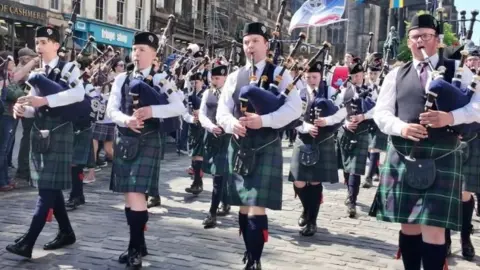 Members of a young pipe band wearing kilts playing as they walk down the Royal Mile, Edinburgh on a sunny day