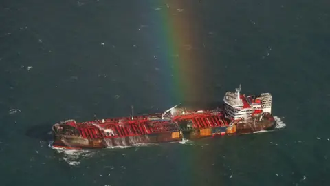 EPA-EFE/REX/Shutterstock Aerial view of the Stena Immaculate showing a hole in the hull of its left side signs of fire damage to the hull and a rainbow above the ship. 