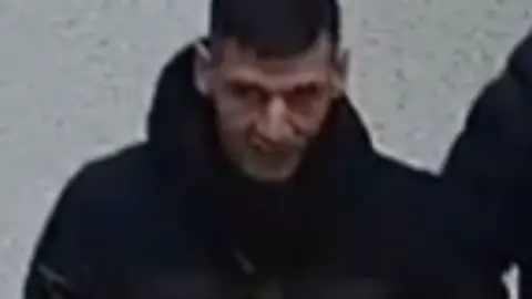 West Yorkshire Police/Morrisons A man with a dark jacket and dark hair taken with a CCTV camera.