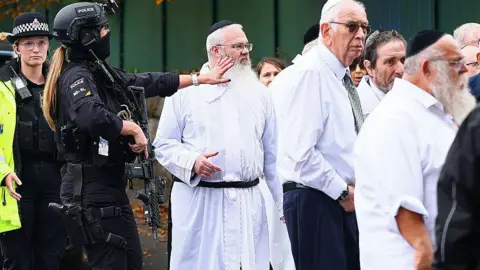 Getty Images Rabbi Daniel Walker, dressed in white, stands among armed police officers outside the synagogue