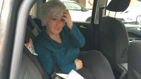 Family Photograph Monica is sitting in the back seat of a car, the photo has been taken from someone at outside the car looking in. She has black leggings on and a teal top. 