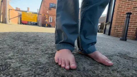 Robert's bare feet standing on a rough surface with lots of loose gravel