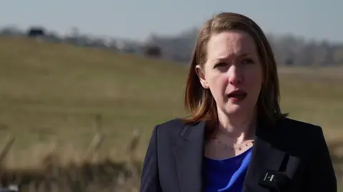 Det Ch Insp Bryony Midgley with brown bobbed hair wearing a black suit jacket and blue top standing in a field in Kirkham.