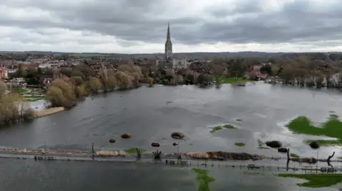 An aerial shot of Salisbury, a cathedral can be seen in the distance. A large field is submerged in water.