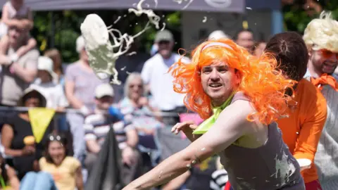 PA Media A man in an orange wig is throwing custard pies.