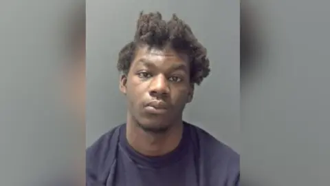 A custody picture of Leon Bangura. He is looking directly at the camera and is wearing a dark pullover.