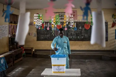 MARCO LONGARI / AFP / GETTY IMAGES A voter casts his ballot at Primary School d'Ekoudou. Colourful paper cut-outs made by children hang from the classroom ceiling. 