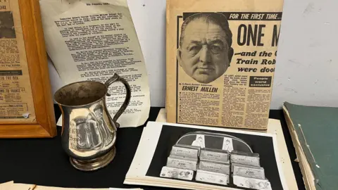 Memorabilia from DCS Millen's police career including a photograph of recovered money from The Great Train Robbery, a commemorative Flying Squad silver tankard and a newspaper article