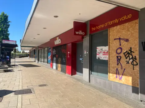 Owen Sennitt/BBC A department store with red branding for the company Wilko can be seen, with boarded up windows and doors, under the canopy over the public pavement.