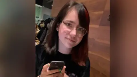 Family handout Teenage girl with long dark shiny hair and a gentle smile. She is wearing cool green nail polish and holding a mobile phone.
