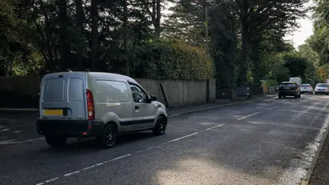 Cars on the road with trees overhead.