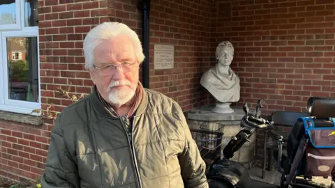 Derek Martin stands outside the common room at Huggens College in Northfleet with his mobility scooter in the background