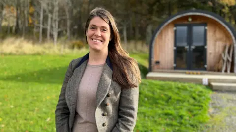 Businesswoman Margot Smolenska smiling at the camera outside a small wooden pod