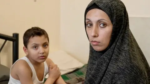 A young boy wears a white jacket and a woman in the veil