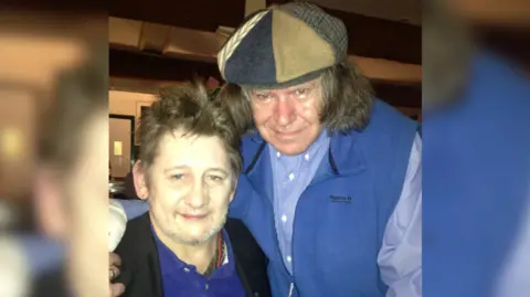 Richie Kavanagh A picture of two men looking at the camera, one is wearing a black jacket and blue polo the other wearing a blue a shirt shirt and blue gilet with a brown and navy flat cap