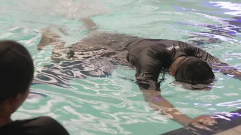 A man is holding the edge of the swimming pool. His face is under the water.